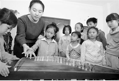 10月11日,在河北省邢臺市橋東區三義廟社區“兒童之家”,小女孩張佳欣在邢臺華藝音樂培訓機構教師楊賽男的指導下感知古箏。